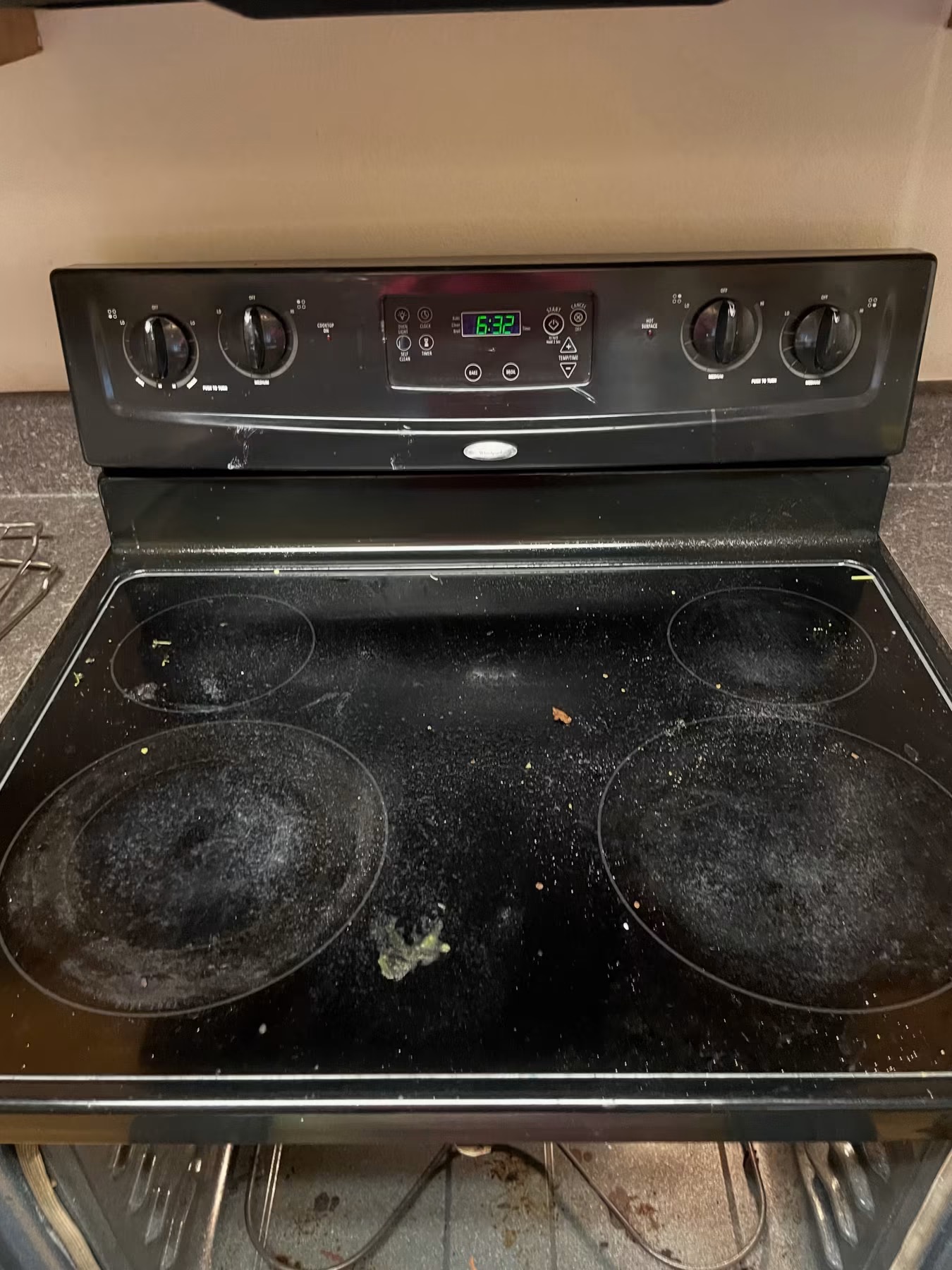 Before cleaning: black glass stovetop covered in burnt food debris, crumbs and grease splatter
